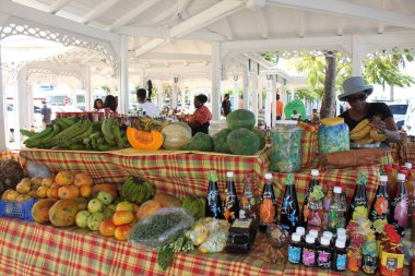 Marigot, Saint Martin, France- November 26, 2016: Local atmosphere at Marigot Market. Stall with exotic fruits, vegetables and traditional specialities. Saleswomen is weihing out a bundle of bananas. clipart