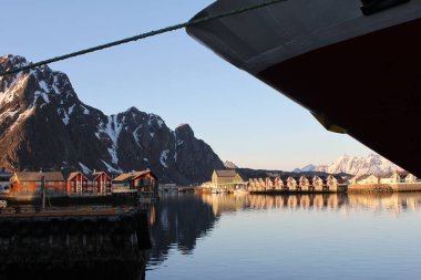 Svolvaer, Norveç-17 Nisan 2019: Hurtigruten gemisi MS Kong Harald 'ın Svolvaer, Lofoten limanında kırbaçlanan pruvasının altında manzara. Günbatımı, balıkçı tekneleri, kaya duvarları, karlı dağ zirveleri.