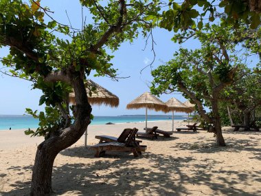 Güney Tayvan 'ın sahil şeridindeki güzel kumsalda güneşlik ve saman kaplı şemsiye çerçeveli. Tropikal bölgede deniz tatili.