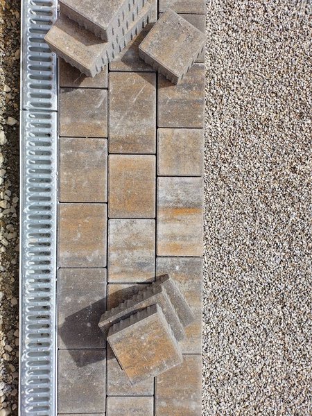 Вертикальное изображение крупного плана дренажа и мощения. Сваленные камни ждут, когда они поместятся в выпрямленный гравий. Солнечный день на стройке.