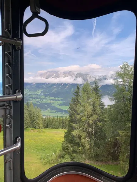 stock image ramic view of the mountains of Dachstein mountain range in Styria (Steiermark) Austria, green ski slope in summer, conifers and blue sky. Seen from curved gondola window of Schladming Tauern cable car at Hauser Kaibling.