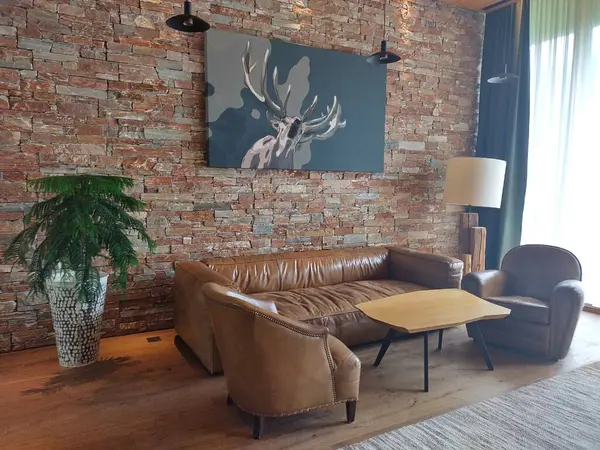 stock image Schladming, Austria, July 12, 2024: Interior of fireplace room at Falkensteiner Hotel Schladming. Atmospheric, stylish designed interior with deer art hanging on brick wall. Brown color scheme.