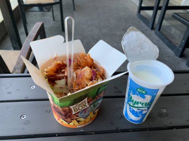 Viyana, Avusturya, 18 Temmuz 2024: Türk fast food 'unun kapatılması, açık hava yemek alanındaki bir masaya ayran yoğurt içeceği konmuş tek kullanımlık konteynır kebap kutusu. Dikey olarak yerleştirilmiş plastik çatal.
