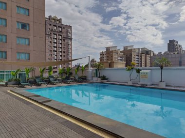 Kaohsiung, Tayvan, 24 Mart 2024 Kaohsiung City 'deki Howard Plaza Oteli' nde çatı yüzme havuzu. Sudaki palmiye ağaçlarının ve gökdelenlerin yansıması..
