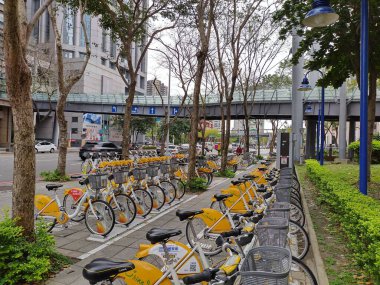 New Taipei City, Taiwan- March 27, 2024: Popular rental bikes (U Bikes) parked in line at busy street in Banqiao District. Traffic rushing by. Environmental friendly transport, mobility in the city. clipart