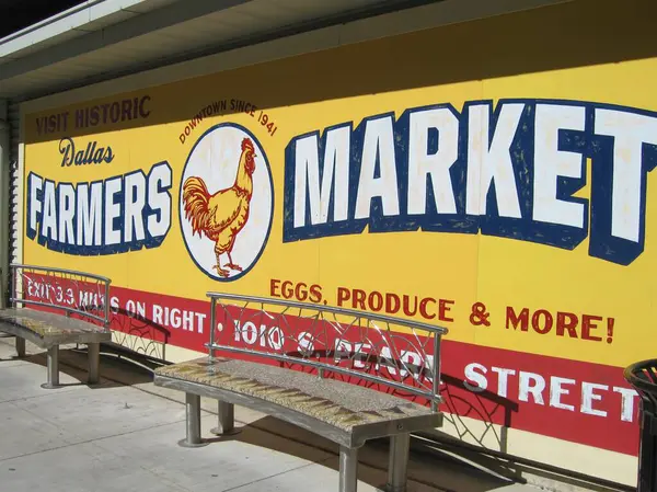 stock image Dallas, Texas, US, October 29, 2017: Colorful designed retro advertisement in bright yellow and red for Dallas Farmers Market with picture of rooster at bus shelter with benches. Sunny day, nobody.