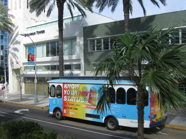 stock image Miami, FL, USA, February 11, 2020:  Trolley in Miami Beach, in front of Bhojwani Tower. Built in 1950s, designed by Albert Anis. Art Deco architecture. Originally a bank. Framed by palm trees. 