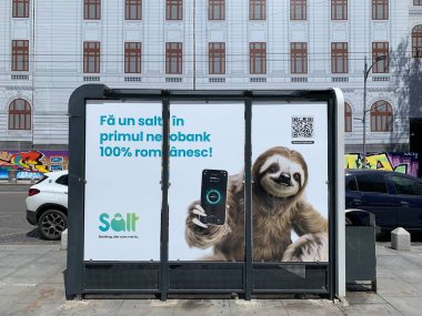 Bükreş, Romanya, 4 Temmuz 2024: Ebankacılık başvurusu için Salt Bank reklamı. Sloth 'un cep telefonu var. Romanya 'nın Bükreş şehir merkezindeki otobüs durağındaki reklam panosu. Güneşli bir gün. Şirin pazarlama konsepti.