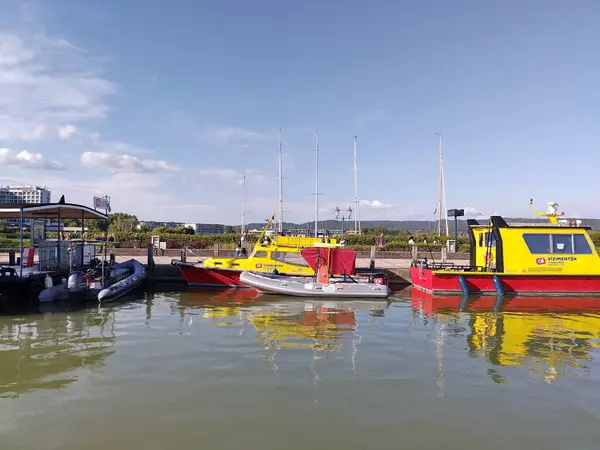 stock image Keszthely, Hungary, August 8, 2024: Red and yellowe lifeguard boats of Hungarian vzimentk docked at marina at lake Balaton. Summertime. Reflection in water.