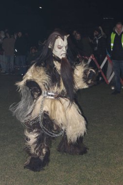 Ganserndorf, Austria - November 23, 2024: Krampus at Perchtenlauf in Austria at night. Horned anthropomorphic figures. Central and Eastern Alpine folkloric tradition. Vertical. Crowd in background.  clipart