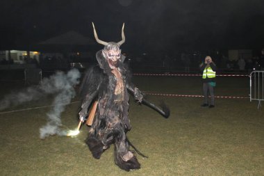 Ganserndorf, Avusturya - 23 Kasım 2024: Krampus, Avusturya 'da düzenlenen geleneksel Perchtenlauf etkinliğinde arenaya yanan meşaleyle giriyor. Arka planda engeller ve kadın fotoğrafçılar.