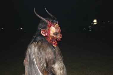 Ganserndorf, Austria - November 23, 2024: Side view of horror fantasy costume of Krampus at Austrian Perchtenlauf at night. Central and Eastern Alpine folkloric tradition in Advent. Scarry costume. clipart