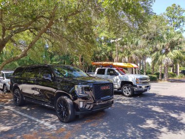 Hilton Head Adası, SC, ABD 24 Eylül 2024: Güneşli bir günde Coligny Beach Park 'taki otoparkta büyük Amerikan kamyonları. Chevrolet çatıda kano taşıyor. Palmiye ağaçları. Seyahat ve eğlence etkinlik teması