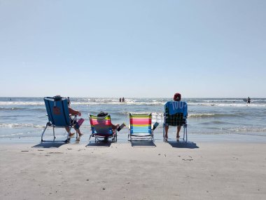 Hilton Head Adası, SC, ABD 24 Eylül 2024: İnsanlar kıyıda büyük su savaşları yapan sandalyelerde oturup okyanusa bakıyorlar. Tatildeki hayatın tadını çıkar. Hilton Head Adası 'nda güzel bir plaj günü.