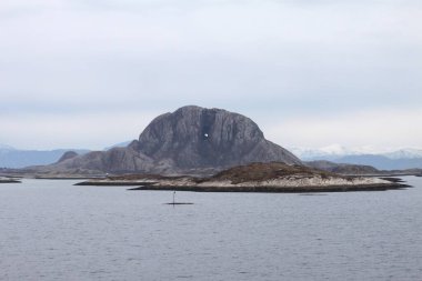 Cruising Arctic sea at the Norwegian coast line by post ship Hurtigruten. View from rear of ship to Torghatten mountain with huge natural hole. Near Torget Bronnoy. Daytime in spring. clipart