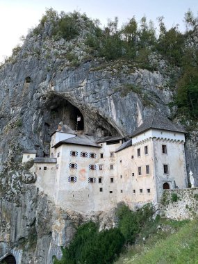 Predjama, Slovenya - 19 Eylül 2019: Mağara ve etrafındaki kayalarla Predjama Kalesi 'ni heyecanlandıran dikey görüntü. Kaya tarafından kucaklanan peri masalı şatosu. Dünyanın en büyük mağara kalesi. Ünlü bir manzara ve ilham verici bir ortam..