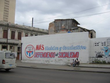 Centro Habana, Havana, Cuba - March 13, 2009: Local young men sitting under muralin Havana city center created by Committees for the Defense of the Revolution CDR stating: 