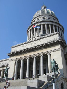 Centro Habana, Havana, Cuba - March 14, 2009: Eastern facade of famous National Capitol of Cuba in Havana, with Cuban flag, steps to main entrance, dome, visitors. Vertical image. Sunny day in spring clipart