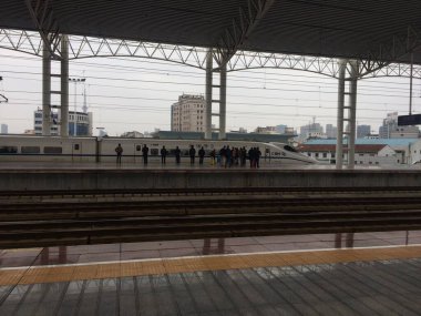 China - March 13, 2017: High-speed train CRH2C-2062 arrives at platform of typical Chinese railway station. Passengers patiently wait to bord. clipart