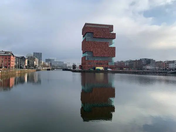 Antwerp, Flanders, Belçika - 09 Ocak 2025: Eilandje 'deki derenin yanındaki ilginç postmodern müze, bulutlu bir kış gününde dalgalı bir liman havzasını yansıtıyor.