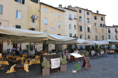 Lucca, Toscana, İtalya - 01 Ekim 2021: Piazza dell 'Anfiteatro' daki açık hava kafeleri, eski bir Roma amfitiyatrosunun kalıntıları üzerine inşa edilmiş bir konut bloğu..