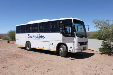 Namibia - March 10, 2018: Medium off-road Mercedes coach operated by Sunshine Tours with open driver's door parked on gravel and dirt. clipart