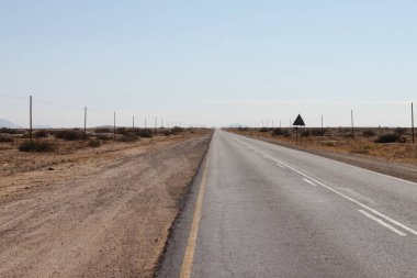 Namibia - March 15, 2018: Panoramic view of Namibian Savannah with typical tarmac road leading straight to horizon. clipart