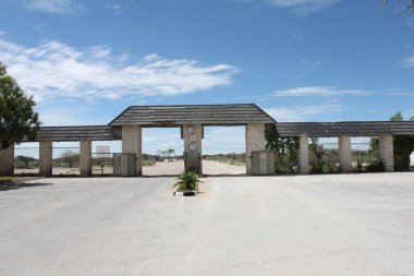 Etosha National Park, Namibia - March 17, 2018: Huge entrance and exit gate at Okaukuejo with clocks showing opening and closing hours depending on season, sunset and sunrise.  clipart