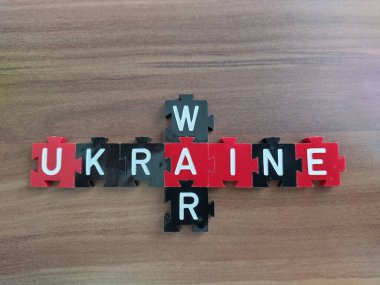 Close-up of the words: Ukraine and War written in white colored board game letters on red and black tokens on wooden background in crossword style.  clipart