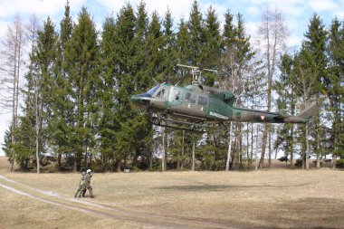 GUePl Geyerhof, St. Peter, Yukarı Avusturya - 12 Mart 2025: Avusturya Hava Kuvvetleri Agusta Bell AB-212 'ye yaklaşan helikopter yerden yükseliyor ve yer ekibi kancaya kargo halatı takıyor.