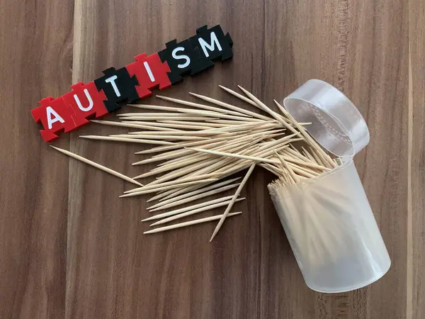 Kelime Otizmi, tahta zeminde kırmızı ve siyah jeton üzerine düşen kürdanlarla tahta oyun harfleriyle yazılmıştır. 80 'lerden bir filme gönderme yaparak farkındalığı artırmak: Otizm bir tabu değildir!