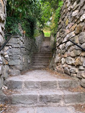 Capital Hill 'den Macaristan' daki Esztergom Bazilikası 'na uzanan eski ve dar bir patika. Taştan yapılmış tarihi duvarlarla çevrili. Yapraklarla çerçevelenmiş. Yaz günü. Etrafta kimse yok. Dikey görünüm.