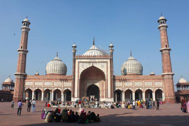 Yeni Delhi, Hindistan - 7 Mart 2019: Hayret verici Jama Camii 'nin gölgesinde minareleri ve şehir merkezindeki kubbeleriyle ibadet edenler oturuyor.