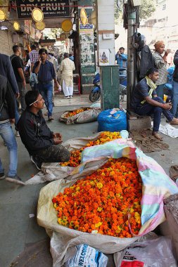 Yeni Delhi, Hindistan - 7 Mart 2019: Diz çökmüş bir sokak satıcısı geçen müşterilere satılmak üzere renkli çiçeklerle dolu çuvallar sunuyor.