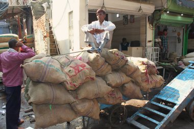 Yeni Delhi, Hindistan - 7 Mart 2019: Teslimatçılar şehir merkezindeki eski baharat pazarı Khari Baoli 'de çalışırken mola verdiler. Egzotik baharatlarla dolu çantalara yaslanmış ve oturuyorlar..