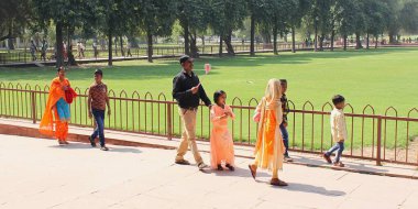 Yeni Delhi, Hindistan - 7 Mart 2019: Sari giyimli yerli turist ailesi Kızıl Kale bahçesinde geziniyor. Babam akıllı telefonu için selfie çubuğuyla donatılmıştı..