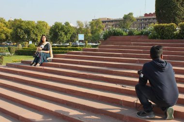 Yeni Delhi, Hindistan - 7 Mart 2019: Mikrofonlu Kadın Şehir Postası muhabiri ön planda kameramanla birlikte aşağı doğru çekilen canlı çekim sırasında geleneksel bir elbise giyerek merdivenlerde oturuyor.