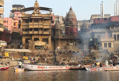 Varanasi, Uttar Pradesh, Hindistan - 13 Mart 2019: Ganj Nehri 'nden seyredilen Harishchandra Ghat' te yaşam ve ölüm. Yakacak odun yığınları, tekneler ve küllerle kaplı binalar..