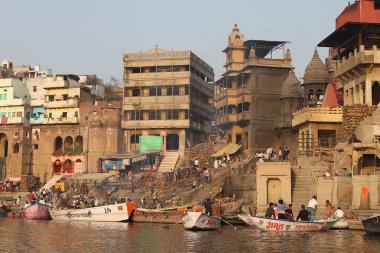 Varanasi, Uttar Pradesh, Hindistan - 13 Mart 2019: Ganj Nehri 'nden seyredilen Harishchandra Ghat' te yaşam ve ölüm. Yakacak odun yığınları, tekneler ve küllerle kaplı binalar..