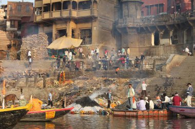 Varanasi, Uttar Pradesh, Hindistan - 13 Mart 2019: Ganj Nehri 'nden seyredilen Harishchandra Ghat' te yaşam ve ölüm. Yakacak odun yığınları, tekneler ve küllerle kaplı binalar..