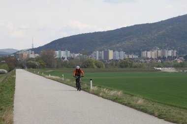 Marchegg, Gaenserndorf, Aşağı Avusturya - 05 Nisan 2025: Slovakya ile Avusturya arasında arka planda Bratislava 'nın etekleriyle iyi korunan bisiklet sürücüsü.