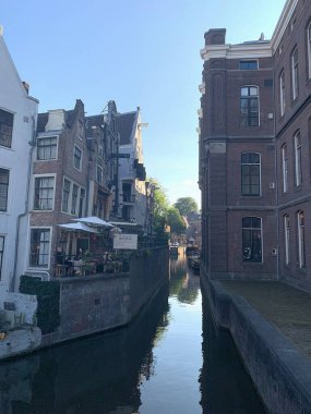 Amsterdam, Hollanda - 15 Eylül 2023: Amsterdam Gracht Grimburgwal 'da deniz kenarındaki gizli restoran bahçesinin gölgesinde oturanlar görülüyor. Yazın sonlarında güneşli bir gün. Güzel evler.