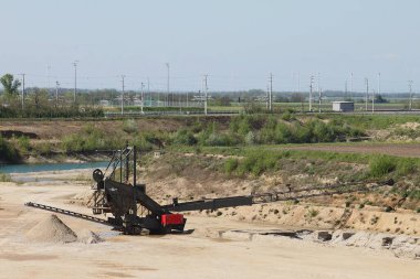 Lassee, Gaenserndorf, Aşağı Avusturya - 20 Nisan 2025: Kazı araçlı tipik açık çakıl ocağı. Yeni gölet yeraltı suyuyla oluşur. Arka planda Lassee Bahnhof tren istasyonu.