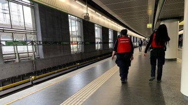 Viyana, Avusturya - 17 Nisan 2025: Üniformalı ve yazılı kırmızı ceketli kadın güvenlik görevlileri Spittelau metro istasyonu platformunda.