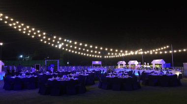 Dubai, Birleşik Arap Emirlikleri - 10 Aralık 2018: Dışarıda büyüleyici bir şekilde hazırlanmış şenlik masası, ışık çelenkleri, sandalyelerin üzerindeki koyu örtüler, mutlak düzen. Şefler ve garsonlarla dolu bir büfe..