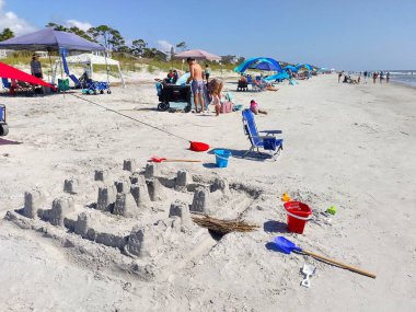 Hilton Head Adası, SC, ABD 24 Eylül 2024: Güneşli bir yaz gününde Hilton Head Adası 'ndaki Coligny Beach Park' ın kumunda büyük bir kumdan kale inşa edildi. İnsanlar güzel havayı, güneşlenmeyi ve yüzmeyi severler.