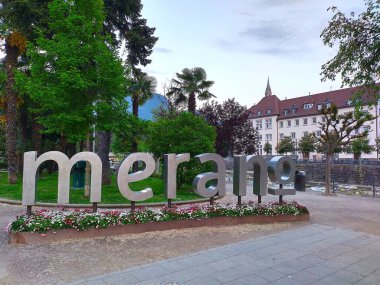 Merano, İtalya 2 Mayıs 2025: Meran veya Merano şehir merkezinde büyük Merano işareti. İlkbaharda Kurpromenade of River Passer 'de (İtalyanca: Passirio). Çiçek süsleme. Seyahat teması