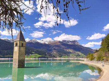 Alt Graun (Vecchio Curon), Vinschgau, Trentino, Güney Tyrol, İtalya - 1 Mayıs 2025: Suni Reschen Gölü 'ndeki (Reschensee, Lago di Resia) sualtı kilise kulesinin çerçeve manzarası. Arka planda güzel alp manzarası.