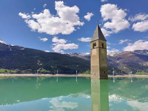Alt Graun (Vecchio Curon), Vinschgau, Trentino, Güney Tyrol, İtalya - 1 Mayıs 2025: Reschen Gölü 'nde (Reschensee, Lago di Resia) sular altında kalmış 14. yüzyıl kilisesi manzarası. Güzel bir dağ manzarası. Baharda güneşli bir gün. Güzel alp manzarası