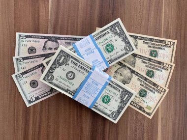 Viyana, Avusturya - 14 Mayıs 2025: Gıcır gıcır bir tomar Amerikan doları banknotunun yanı sıra beş ve on dolarlık banknotlar. BEP gravür ve baskı bürosu tarafından yeni üretildi. Ahşap arka planda $.